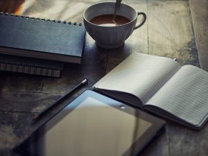 Fortsetzung schreiben; gemütlicher Tisch mit Kaffee, Notizbüchern, Stift und Tablet, Blog